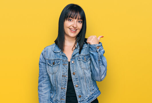Young hispanic woman wearing casual clothes smiling with happy face looking and pointing to the side with thumb up.