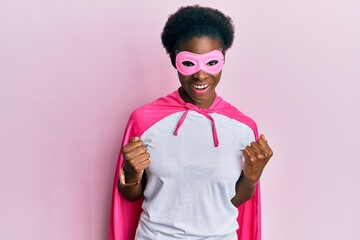 Young african american girl wearing superhero mask and cape costume celebrating surprised and amazed for success with arms raised and open eyes. winner concept.