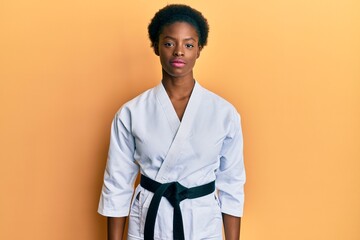 Young african american girl wearing karate kimono and black belt relaxed with serious expression on...