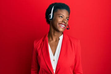 Young african american girl wearing call center agent headset looking away to side with smile on...