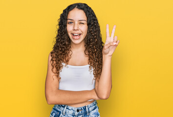 Teenager hispanic girl wearing casual clothes smiling with happy face winking at the camera doing victory sign. number two.