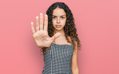 Teenager hispanic girl wearing casual clothes doing stop sing with palm of the hand. warning expression with negative and serious gesture on the face.
