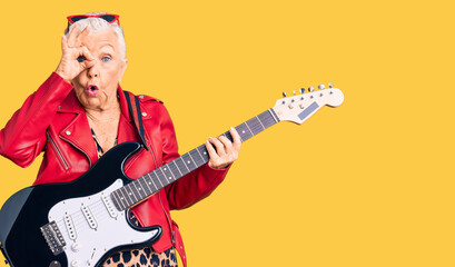 Senior beautiful woman with blue eyes and grey hair wearing a modern look playing electric guitar doing ok gesture shocked with surprised face, eye looking through fingers. unbelieving expression.