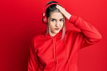 Young modern girl wearing gym clothes and using headphones confuse and wonder about question. uncertain with doubt, thinking with hand on head. pensive concept.