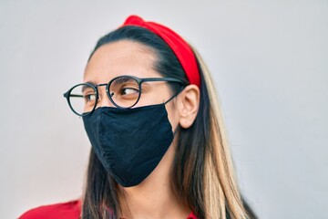 Young hispanic woman wearing coronavirus protection mask standing at the city.