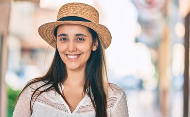 Young hispanic tourist woman wearing summer hat standing at the city.