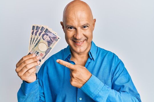 Middle age bald man holding 5000 japanese yen banknotes smiling happy pointing with hand and finger