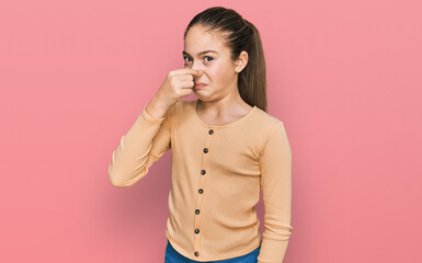 Beautiful brunette little girl wearing casual sweater smelling something stinky and disgusting,...