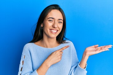 Young hispanic girl wearing casual clothes amazed and smiling to the camera while presenting with hand and pointing with finger.