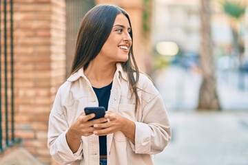 Young hispanic girl smiling happy using smartphone at the city.