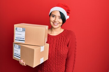 Beautiful young woman with short hair wearing christmas hat holding delivery packages looking positive and happy standing and smiling with a confident smile showing teeth