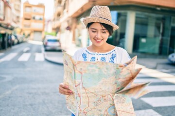Young latin tourist girl on vacation smiling happy holding map at the city.