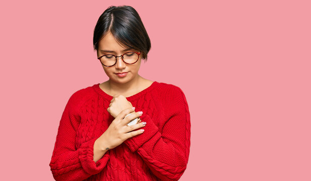 Young beautiful hispanic woman with short hair wearing casual sweater and glasses suffering pain on hands and fingers, arthritis inflammation