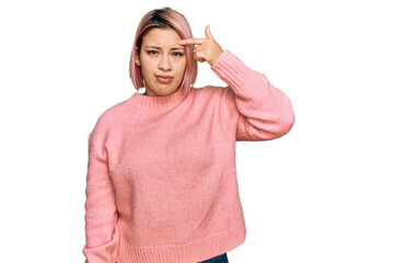 Hispanic woman with pink hair wearing casual winter sweater pointing unhappy to pimple on forehead, ugly infection of blackhead. acne and skin problem