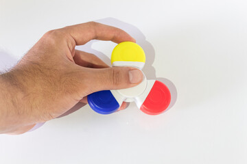 Hand holding a yellow, blue and red fidget spinner without spinning over a white background