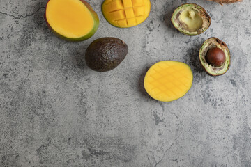 Sliced tropical fruit mango and broken avocado on marble surface