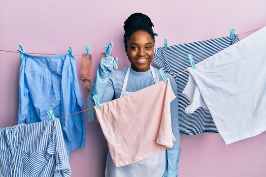 African american woman with braided hair washing clothes at clothesline smiling amazed and surprised and pointing up with fingers and raised arms.