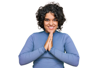 Fototapeta na wymiar Young hispanic woman with curly hair wearing casual clothes praying with hands together asking for forgiveness smiling confident.