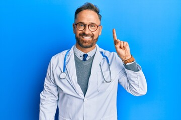 Handsome middle age man wearing doctor uniform and stethoscope showing and pointing up with finger number one while smiling confident and happy.