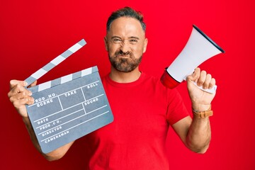 Handsome middle age man holding video film clapboard and megaphone puffing cheeks with funny face....