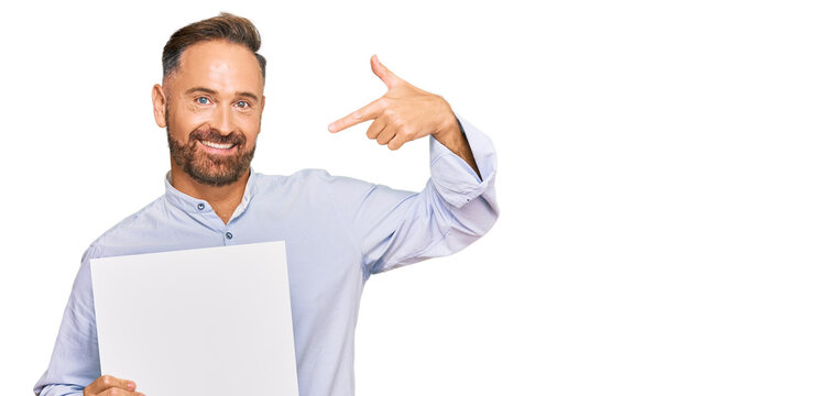 Handsome middle age man holding blank empty banner pointing finger to one self smiling happy and proud