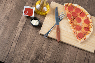 Wide angle photo of Half of pepperoni pizza on wooden plate with sauces and oil