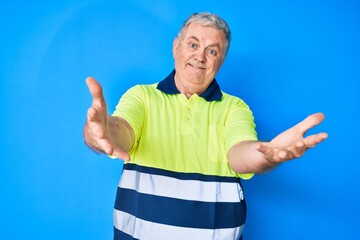 Senior grey-haired man wearing reflective t shirt looking at the camera smiling with open arms for...