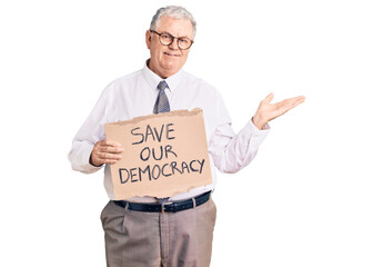 Senior grey-haired man wearing business clothes holding save our democracy protest banner celebrating victory with happy smile and winner expression with raised hands