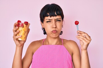 Beautiful brunettte woman eating fresh and healthy fruit puffing cheeks with funny face. mouth inflated with air, catching air.