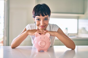 Young brunette woman smiling happy showing proud piggy bank with savings