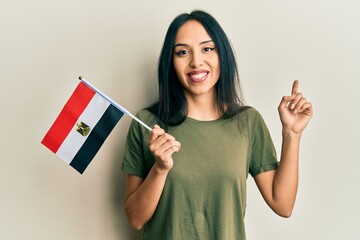 Young hispanic girl holding egypt flag smiling happy pointing with hand and finger to the side