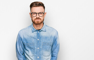Young redhead man wearing casual denim shirt puffing cheeks with funny face. mouth inflated with air, crazy expression.