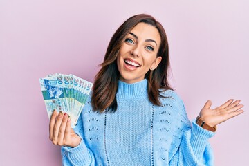 Young brunette woman holding hong kong 20 dollars banknotes celebrating achievement with happy smile and winner expression with raised hand