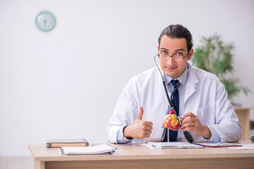 Young male doctor cardiologist listening heart model with stetho