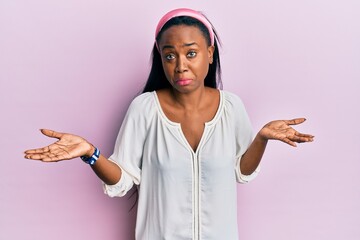 Young african woman wearing casual clothes over pink background clueless and confused expression...