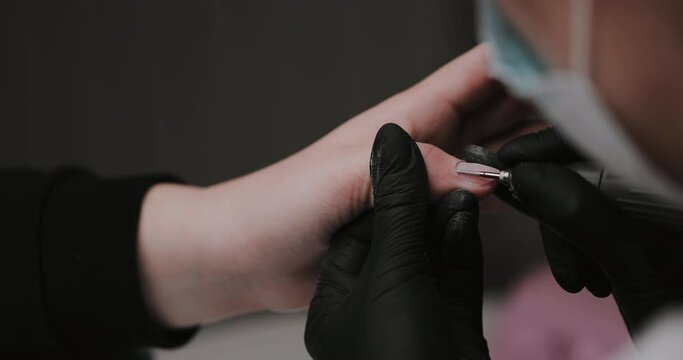 The manicurist cleans the cuticle of the nails with the device. Cuticle removal using a machine with a cutter. Professional manicure in the salon close-up.