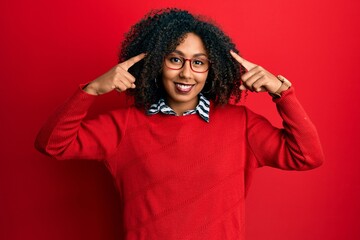 Beautiful african american woman with afro hair wearing sweater and glasses smiling pointing to head with both hands finger, great idea or thought, good memory