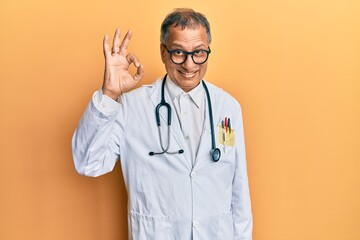 Middle age indian man wearing doctor coat and stethoscope smiling positive doing ok sign with hand and fingers. successful expression.