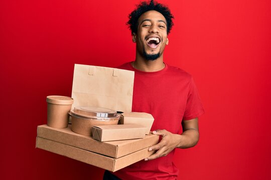 Young african american man with beard holding take away food smiling and laughing hard out loud because funny crazy joke.