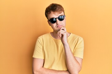 Young caucasian man wearing stylish sunglasses thinking concentrated about doubt with finger on...
