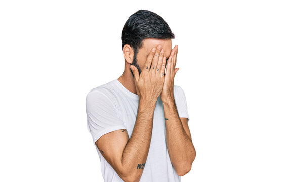 Young hispanic man wearing casual white t shirt with sad expression covering face with hands while crying. depression concept.