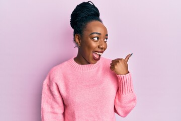 Young african american woman wearing casual winter sweater smiling with happy face looking and pointing to the side with thumb up.