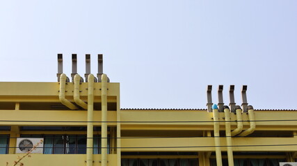 Ventilation ducts on the building roof. Several yellow ducts suck out the air in a laboratory or school building for ventilation on a blue sky background with a copy area. Selective focus