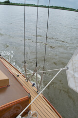 Naklejka premium Detail of the shrouds (side stays) on a sailing yacht, moving at speed on a lake. Jib sheets and cabin top in the foreground; lake shore and waves in the background