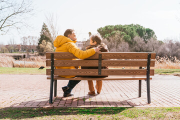 Back view of a lovely happy senior couple sitting on a bench in the park on a sunny winter day