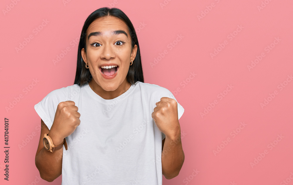 Wall mural Young asian woman wearing casual white t shirt celebrating surprised and amazed for success with arms raised and open eyes. winner concept.