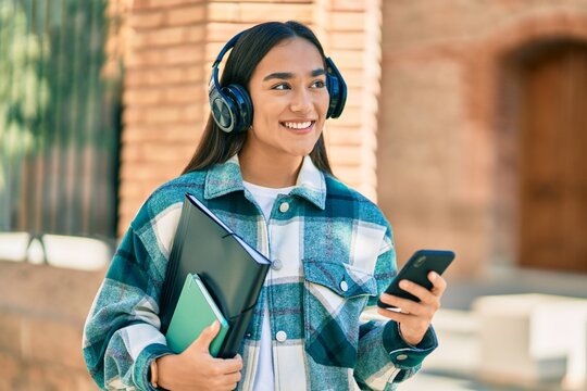 Young latin student girl smiling happy using smartphone and headphones at the city.