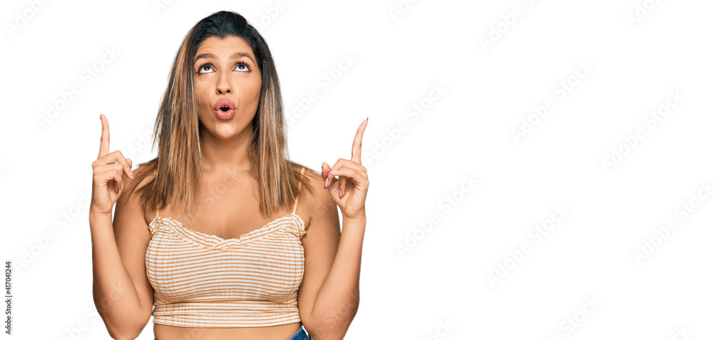 Poster beautiful brunette woman wearing casual clothes amazed and surprised looking up and pointing with fi