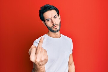 Young hispanic man wearing casual white tshirt showing middle finger, impolite and rude fuck off expression