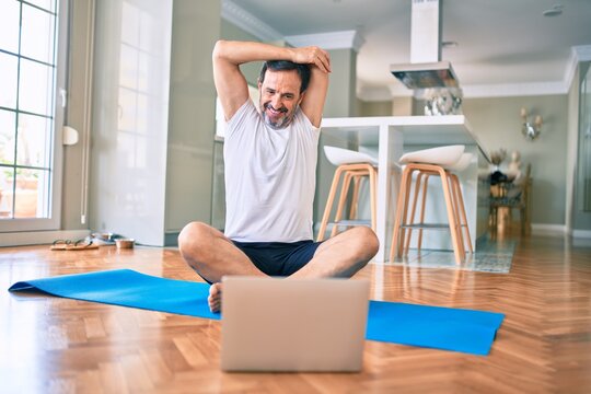Middle age man with beard training and stretching doing exercise at home looking at sport video on computer